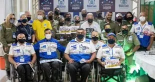 Grupo posa para foto em evento, com pessoas em cadeiras de rodas segurando placas