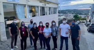 Grupo de pessoas de máscara posando em frente a um prédio, com vista da cidade ao fundo