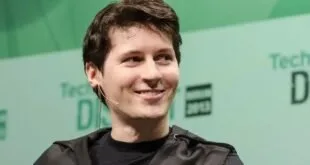 Homem jovem sorrindo diante de painel de um evento de tecnologia