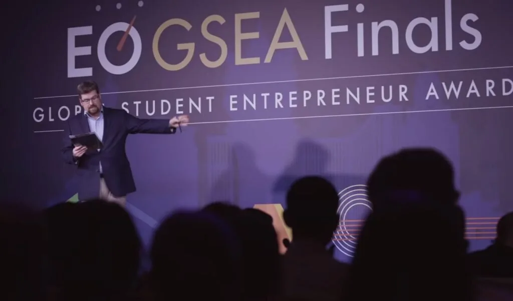 Pessoa em palco diante de telão com os dizeres 'GSEA Final' e 'Student Entrepreneur'