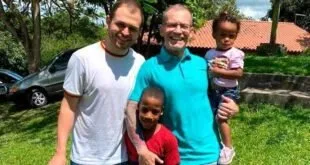 Homens e crianças posando juntos e sorrindo ao ar livre em área com vegetação