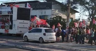 Manifestantes com bandeiras vermelhas reunidos na rua ao lado de um ônibus