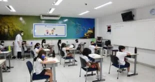 Sala de aula com estudantes uniformizados sentados em carteiras espaçadas