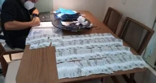 Policial de máscara preenche documento em mesa coberta por notas de duzentos reais
