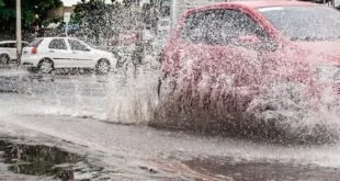 Carros atravessando alagamento em rua e levantando muita água durante chuva forte