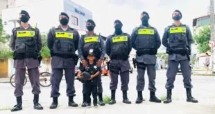 Seis policiais militares fardados posando em rua com criança vestida de policial no centro