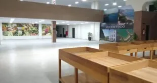 Interior de mercado com bancadas de madeira vazias e painel 'Seja bem vindo' com fotos de praias