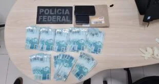 Cédulas de cem reais espalhadas sobre mesa ao lado de distintivo da Polícia Federal e um envelope