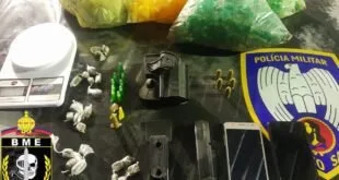 Sacos com entorpecentes, balança e celular apreendidos sobre mesa com brasão da Polícia Militar