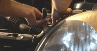 Mãos de mecânico com chave ajustando o farol de um carro com o capô aberto