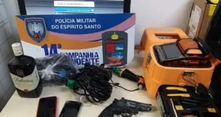 Revólver, celulares e maleta de ferramentas expostos sobre mesa com placa da Polícia Militar