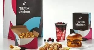 Embalagens de delivery com a marca 'TikTok Kitchen' ao lado de lanche, frango e bebida