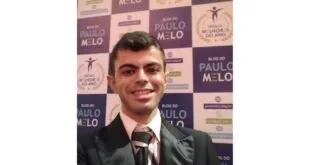 Homem de terno e gravata sorrindo diante de painel com o logotipo 'Blog do Paulo Melo'