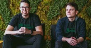 Dois homens sentados lado a lado com camisetas do Rei do Pitaco diante de parede de vegetação