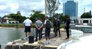 Grupo de homens reunidos em cais à beira d'água, alguns com roupa de mergulho