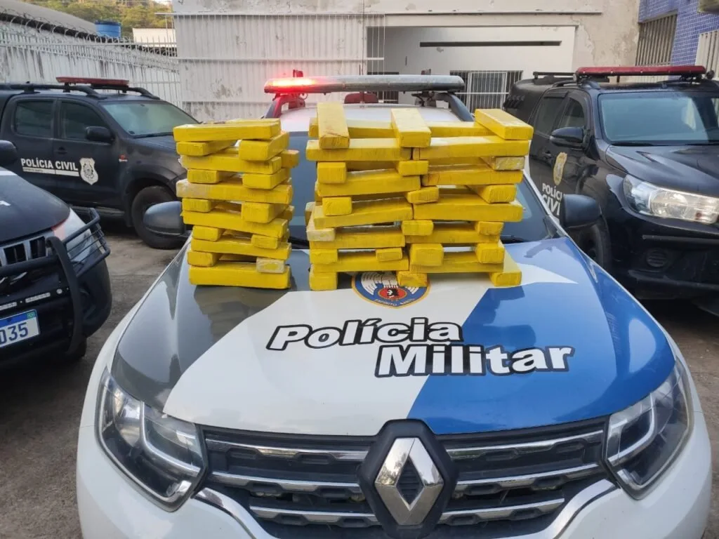 Tabletes de droga empilhados sobre o capô de viatura com a inscrição 'Polícia Militar'