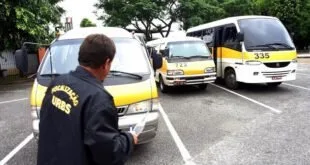 Fiscal uniformizado anota dados diante de vans e micro-ônibus escolares estacionados