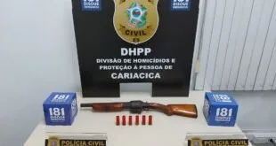 Munições e arma sobre mesa diante de painel da Polícia Civil com a sigla 'DHPP'
