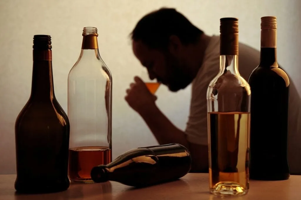 Garrafas de bebida alcoólica sobre mesa com homem desfocado ao fundo, imagem ilustrativa