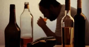 Garrafas de bebida alcoólica sobre mesa com homem desfocado ao fundo, imagem ilustrativa