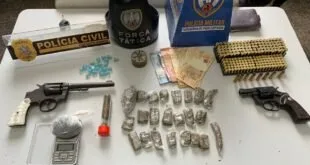 Revólver, munições e porções de droga sobre mesa ao lado de coletes da Polícia Militar