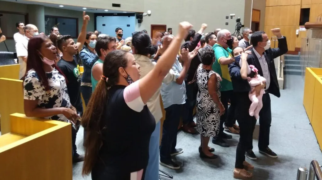Plateia em pé de braços erguidos e punhos cerrados em auditório lotado durante audiência
