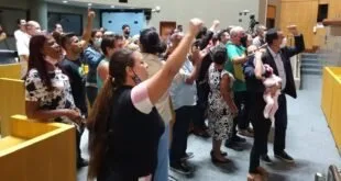 Plateia em pé de braços erguidos e punhos cerrados em auditório lotado durante audiência