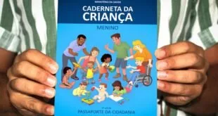 Mão segurando a Caderneta da Criança do Ministério da Saúde com capa azul e desenhos infantis