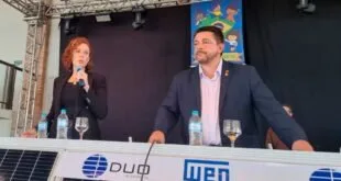 Mulher ao microfone e homem sentados a mesa com placa solar e os logotipos 'DUO' e 'WEG'