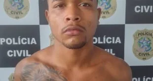 Homem sem camisa e com tatuagem no braço diante de painel com o texto 'Polícia Civil'