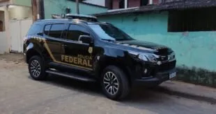 Caminhonete preta da Polícia Federal estacionada em rua diante de muro verde