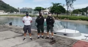 Três homens, dois deles fardados, posam à beira da água com material apreendido no chão
