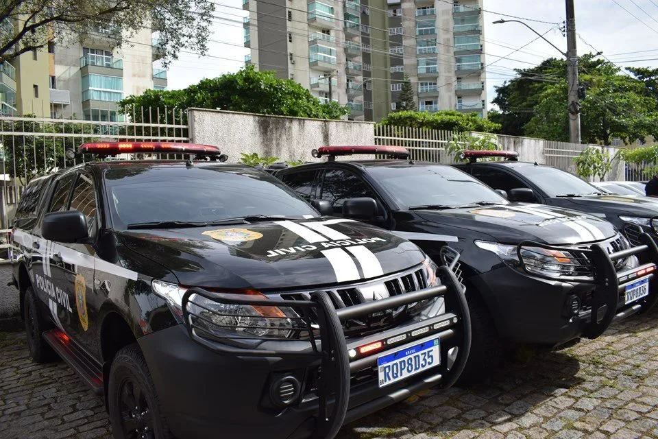 Viaturas pretas da Polícia Civil estacionadas em fila diante de prédio residencial