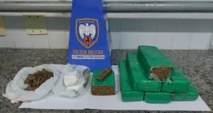Tabletes e porções de droga apreendidos sobre mesa ao lado de bandeira da Polícia Militar