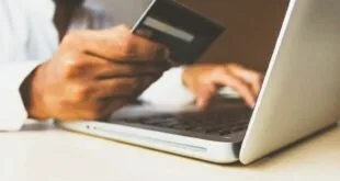 Homem segura cartão de crédito diante de notebook aberto sobre mesa clara
