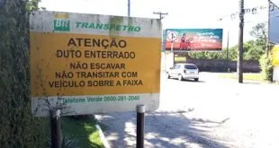 Placa amarela de aviso sobre duto enterrado fixada à beira de uma via