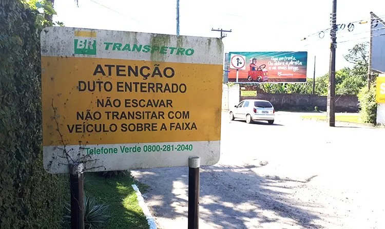Placa amarela de aviso sobre duto enterrado fixada à beira de uma via