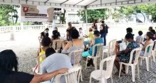 Pessoas de máscara sentadas em cadeiras de plástico aguardam atendimento em área coberta