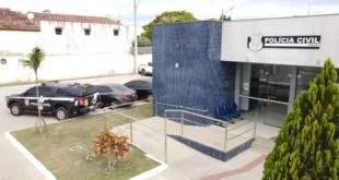 Fachada de prédio público com portão azul e viaturas estacionadas na lateral