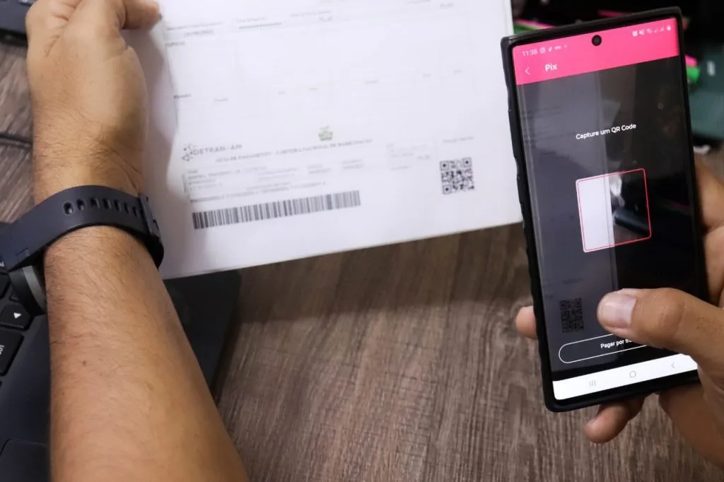 Mão segura celular apontado para o código de barras de um documento impresso sobre a mesa