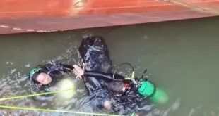 Mergulhador com cilindros de ar na água ao lado do casco alaranjado de um navio