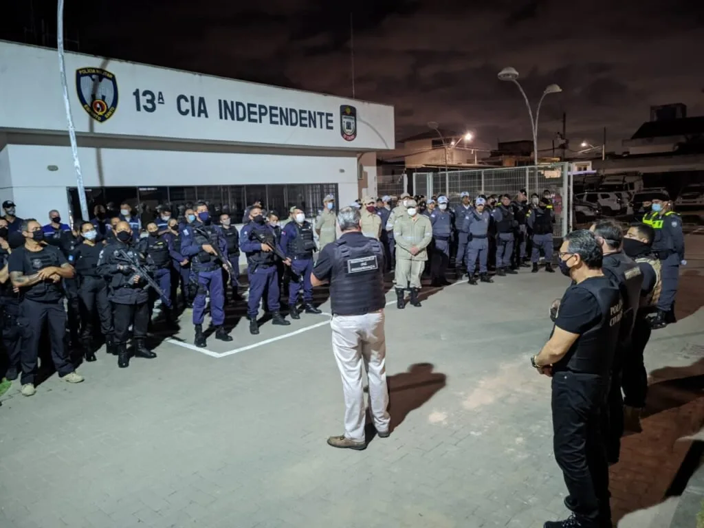 Policiais militares em formação noturna diante de painel com a inscrição '13ª Cia Independente'