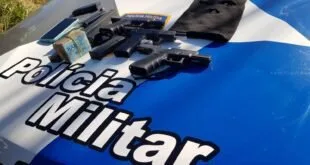 Armas, dinheiro e mochila apreendidos expostos sobre o capô de viatura da Polícia Militar