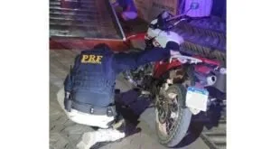 Motocicleta caída no chão ao lado de viatura da PRF durante fiscalização noturna
