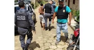 Policiais militares conduzem homem algemado por rua de paralelepípedo em área residencial
