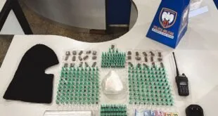 Pinos de droga, touca ninja, rádio comunicador e porção branca apreendidos sobre uma mesa