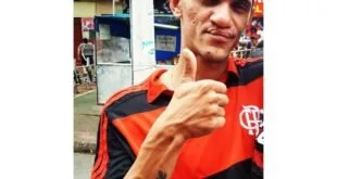 Homem de camisa rubro-negra faz sinal de positivo para a câmera em uma calçada