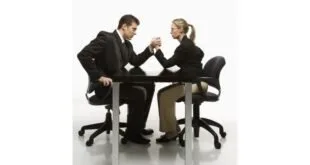 Homem e mulher de terno em queda de braço sobre mesa, imagem ilustrativa sobre carreira