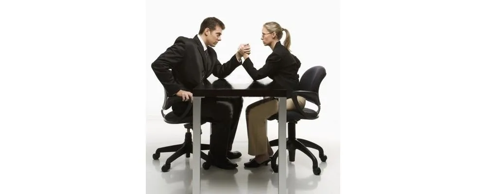 Homem e mulher de terno em queda de braço sobre mesa, imagem ilustrativa sobre carreira