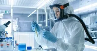 Profissional em traje de proteção completo manuseia pipeta em bancada de laboratório